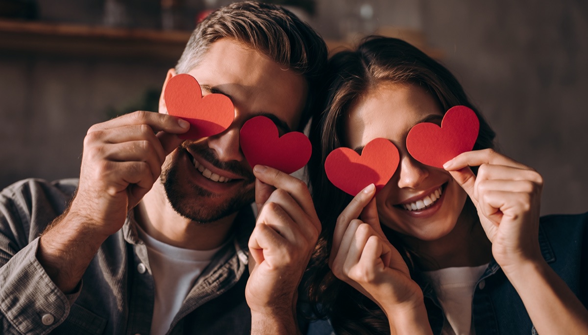Couple holding paper hearts over their eyes
