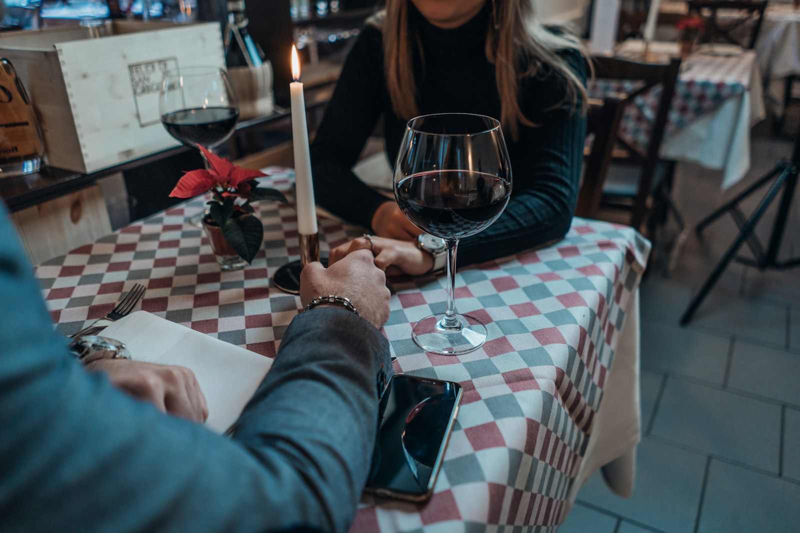 Couple holding hands across a small cafe table with glasses of wine