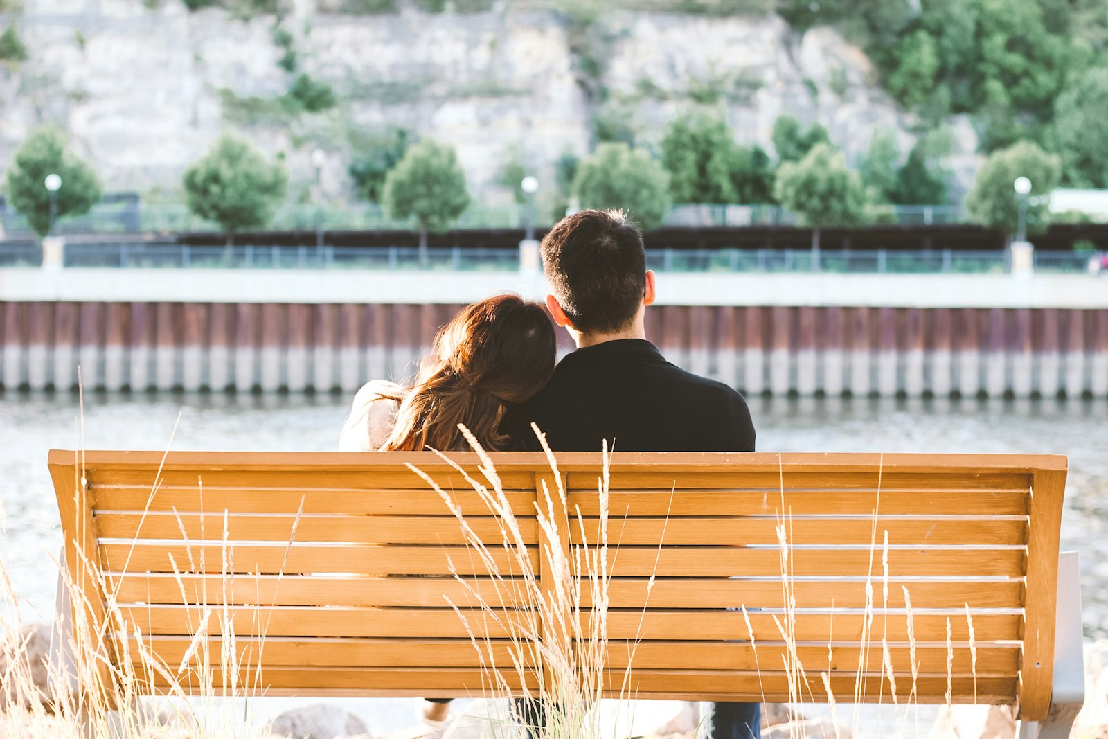 Couple sitting close together on a wooden bench by a river on a sunny afternoon