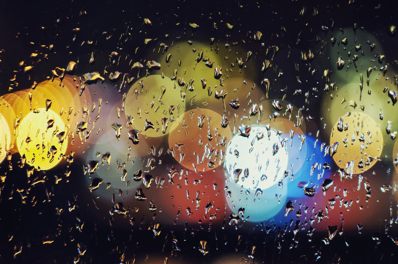 Rain droplets on a window with colorful blurred city lights