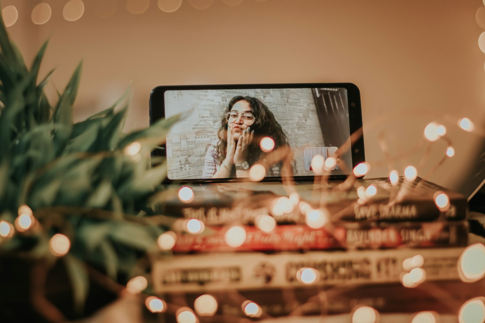 Video call date with a phone propped on books surrounded by string lights